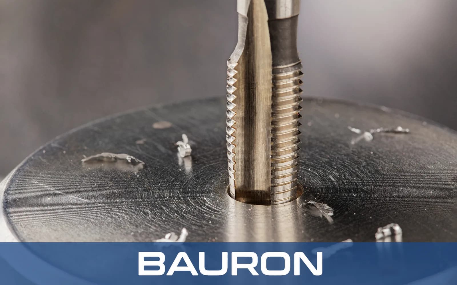 Tap cutting a thread into a steel part with chips around the hole